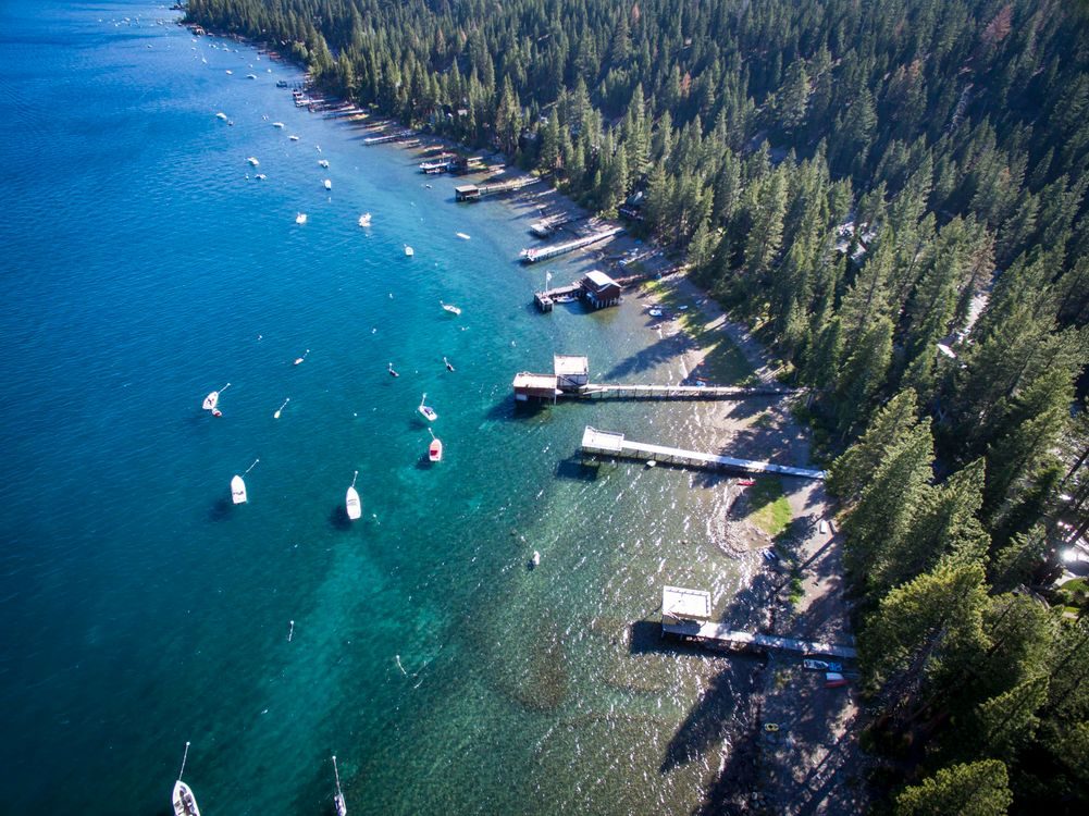 Aerial view of the Lake Tahoe shoreline with boats moored in clear blue water beside pine forest and docks