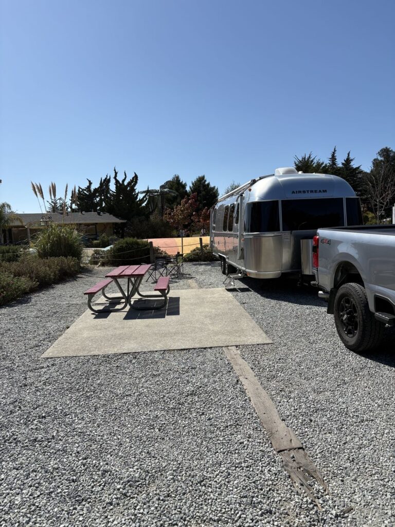 Airstream travel trailer delivered and set up on a KOA campsite near Monterey, tow truck alongside and a picnic table on the pad