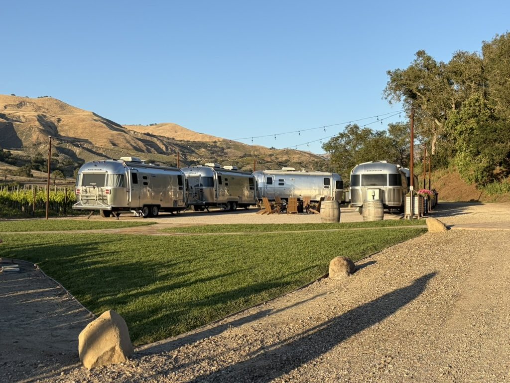 Four GoSilver Airstream trailers lined up under string lights at a vineyard for a group event