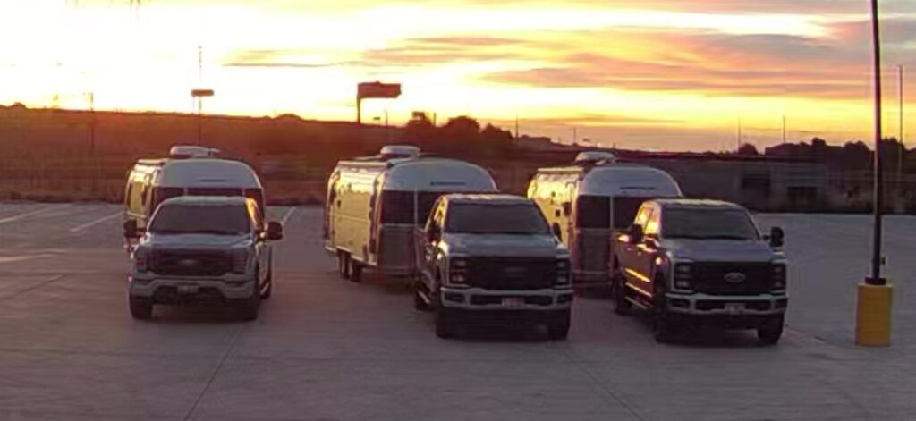 Four Airstream trailers hitched to tow trucks at sunrise, loaded for delivery from the GoSilver lot in Lathrop